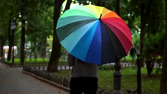 在城市公园的雨天，一个面目全非的女人带着五颜六色的雨伞行走