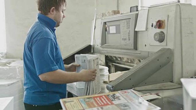 在一家印刷厂，穿着蓝色夹克的工人把纸放在切纸机上，滑块