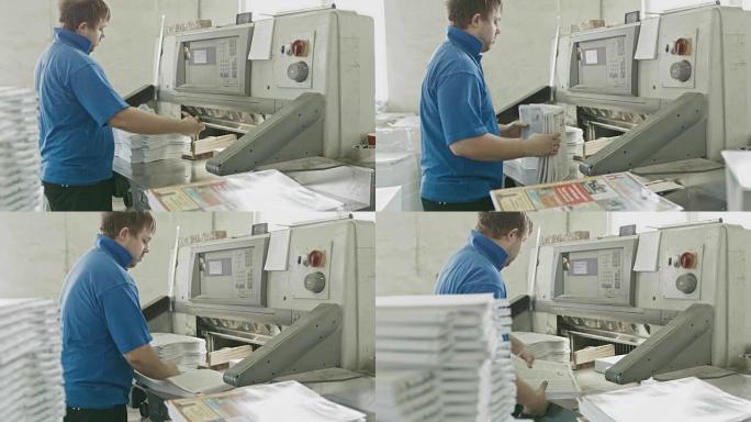 在一家印刷厂，穿着蓝色夹克的工人把纸放在切纸机上，滑块