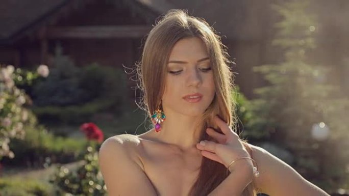性感的长发女孩穿着比基尼微笑着诱人地在花园里移动，玫瑰花在水花下飞溅