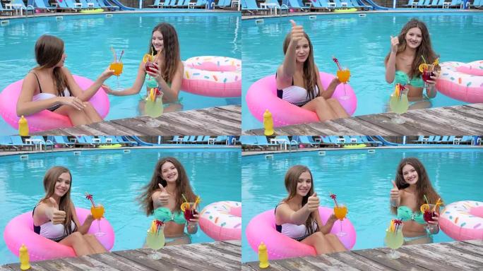 在游泳池度假胜地的年轻女性度过了愉快的假期，手里拿着鸡尾酒的女朋友的积极姿态