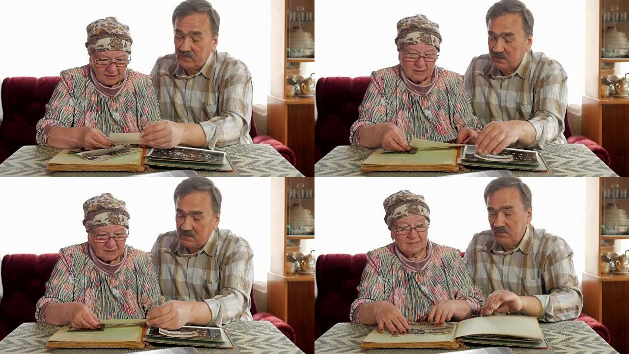 一对老年夫妇正在家里看着他们的旧照片，聊天。有胡子的男人，有眼镜的妻子