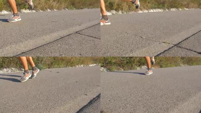 壮汉的脚在夏天的路上奔跑。日落时分，男性在乡村路线上进行慢跑训练。年轻人正在一条空荡荡的柏油路上训练