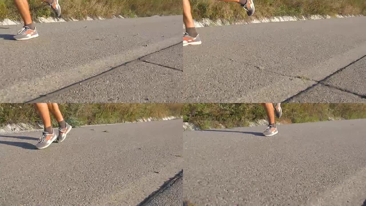 壮汉的脚在夏天的路上奔跑。日落时分，男性在乡村路线上进行慢跑训练。年轻人正在一条空荡荡的柏油路上训练