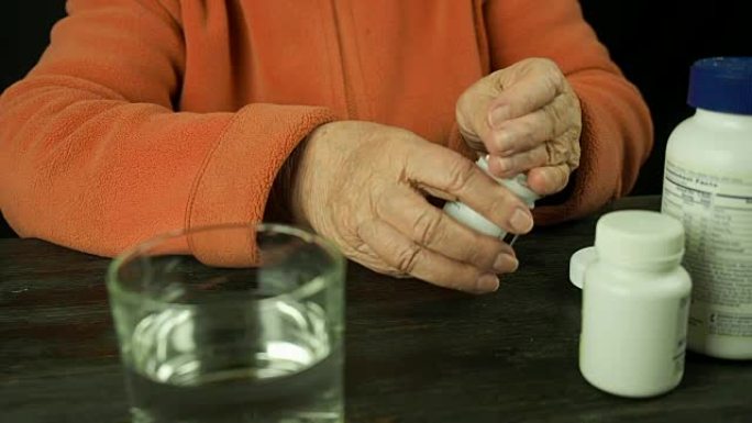 老年妇女的手拿着药片喝水