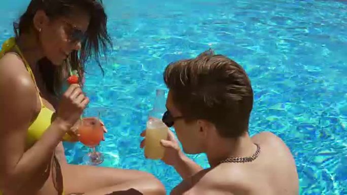 年轻的成年夫妇在游泳池里调情和聊天，喝鸡尾酒。夏季泳池派对。4k拍摄