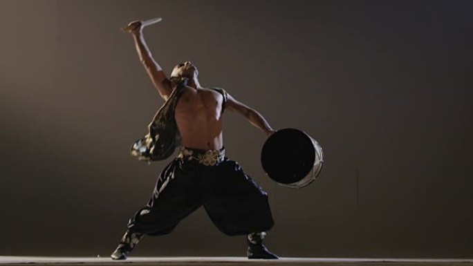 萨满在灰色背景上用鼓跳舞。亚洲民族舞蹈。在慢动作的红色史诗巨龙电影相机上拍摄。