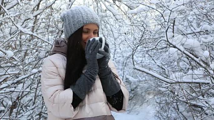 美丽快乐的女孩用热茶热身。冬季公园积雪覆盖的树木