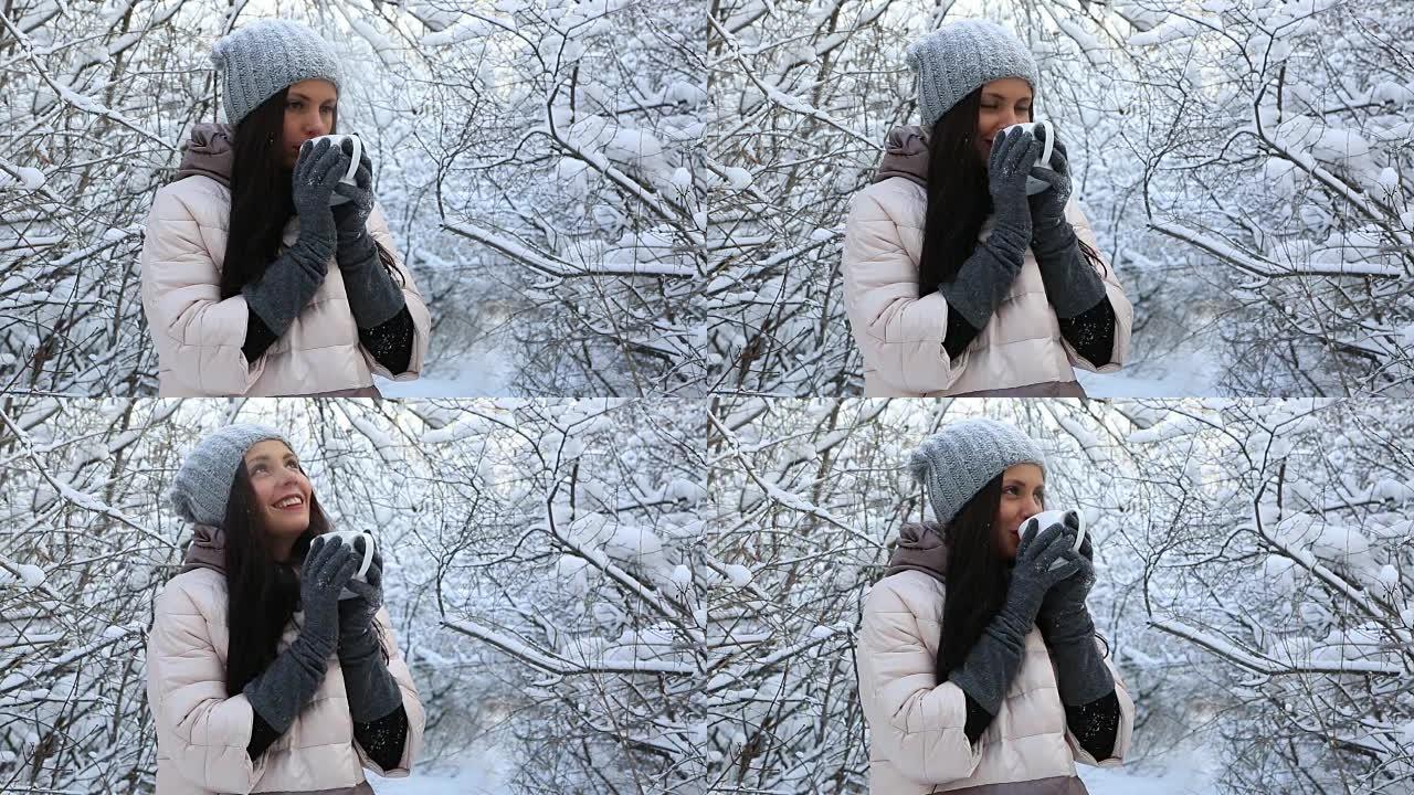 美丽快乐的女孩用热茶热身。冬季公园积雪覆盖的树木