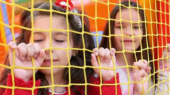 两个女孩抱着充气橡胶城堡游乐场的网。儿童户外娱乐