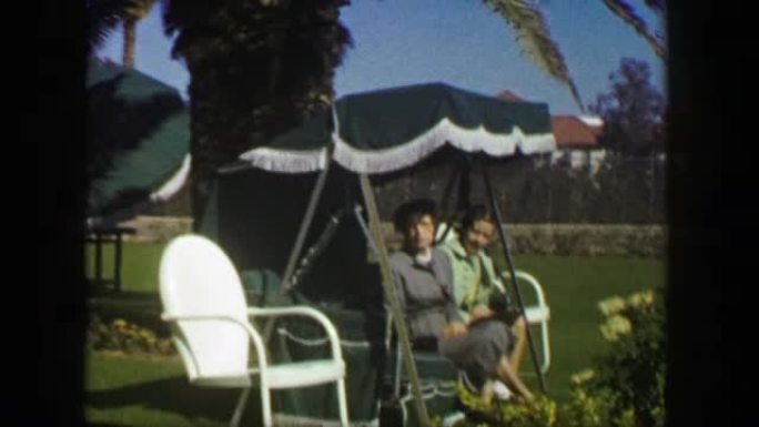 1947: 母女坐户外棕榈树躺椅家具。