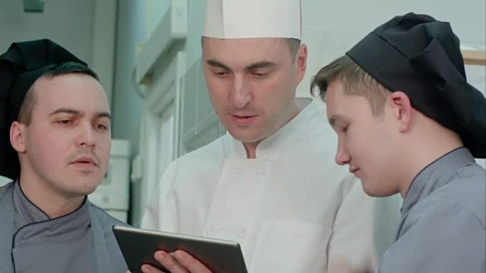 年轻的厨师学员与拿着平板电脑的厨师进行讨论