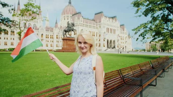 在布达佩斯议会的背景下，年轻女子游客与匈牙利国旗合影。欧洲旅游业