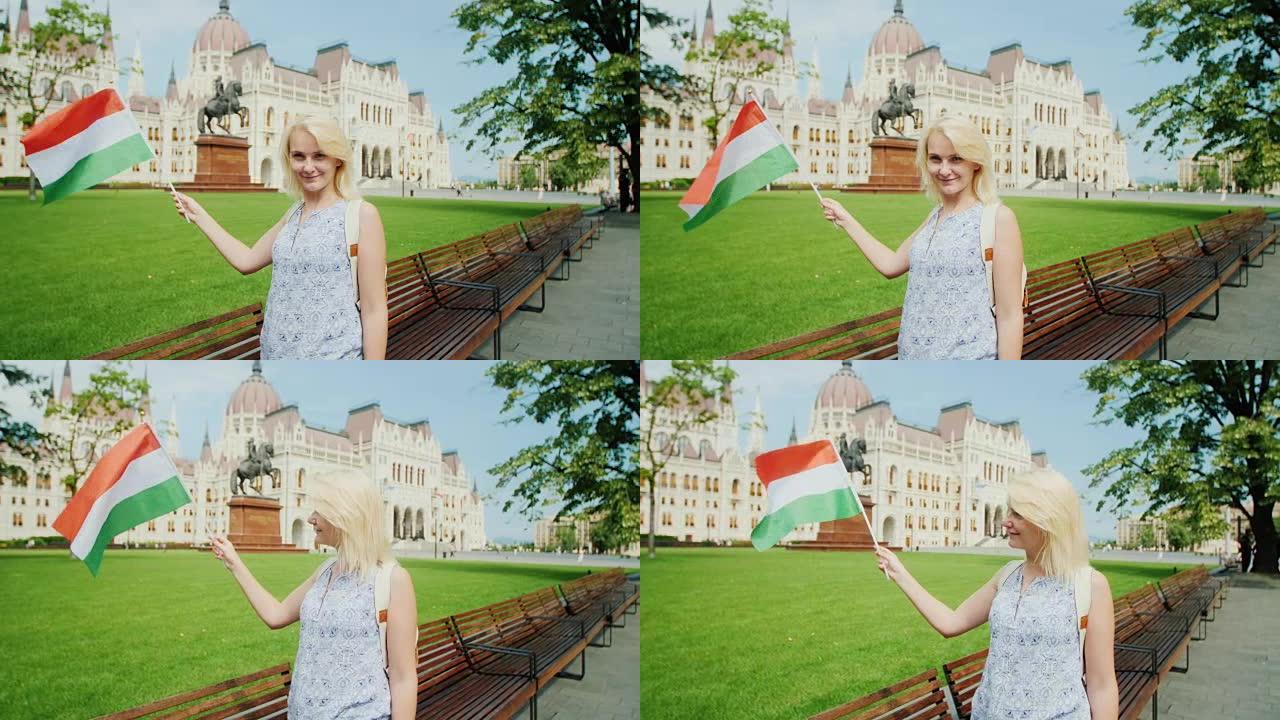 在布达佩斯议会的背景下，年轻女子游客与匈牙利国旗合影。欧洲旅游业