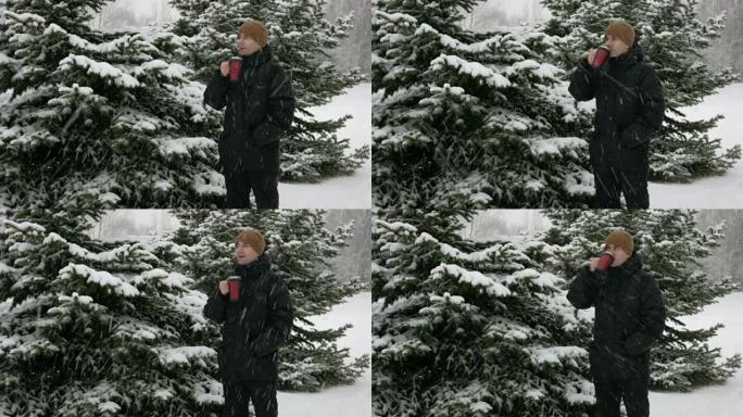 一个年轻人在冬天的森林里从热水瓶里喝热饮料。大雪。该名男子穿着深色外套和保暖帽子在雪地和树木中环顾四