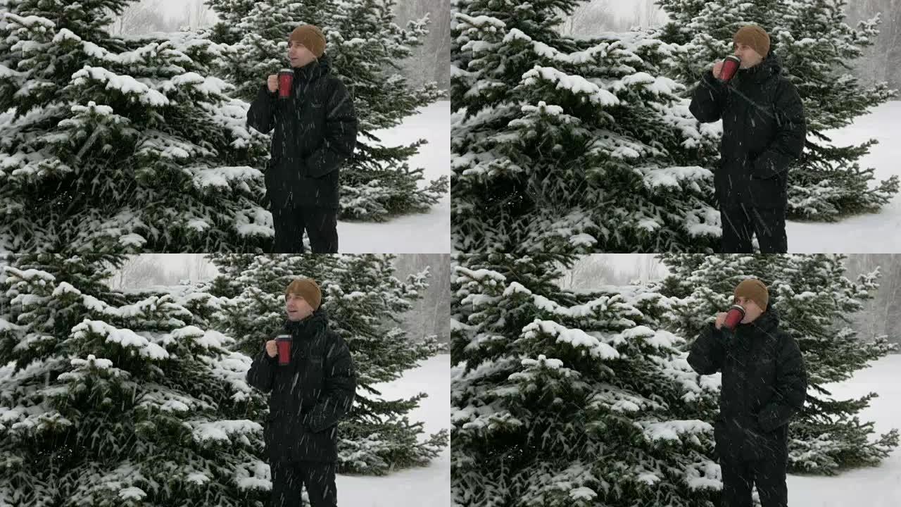 一个年轻人在冬天的森林里从热水瓶里喝热饮料。大雪。该名男子穿着深色外套和保暖帽子在雪地和树木中环顾四