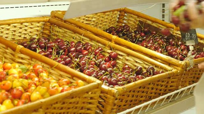 女性的手正在杂货店生产部门拿走新鲜的樱桃，并将其放入塑料袋中。女孩在超市选择水果