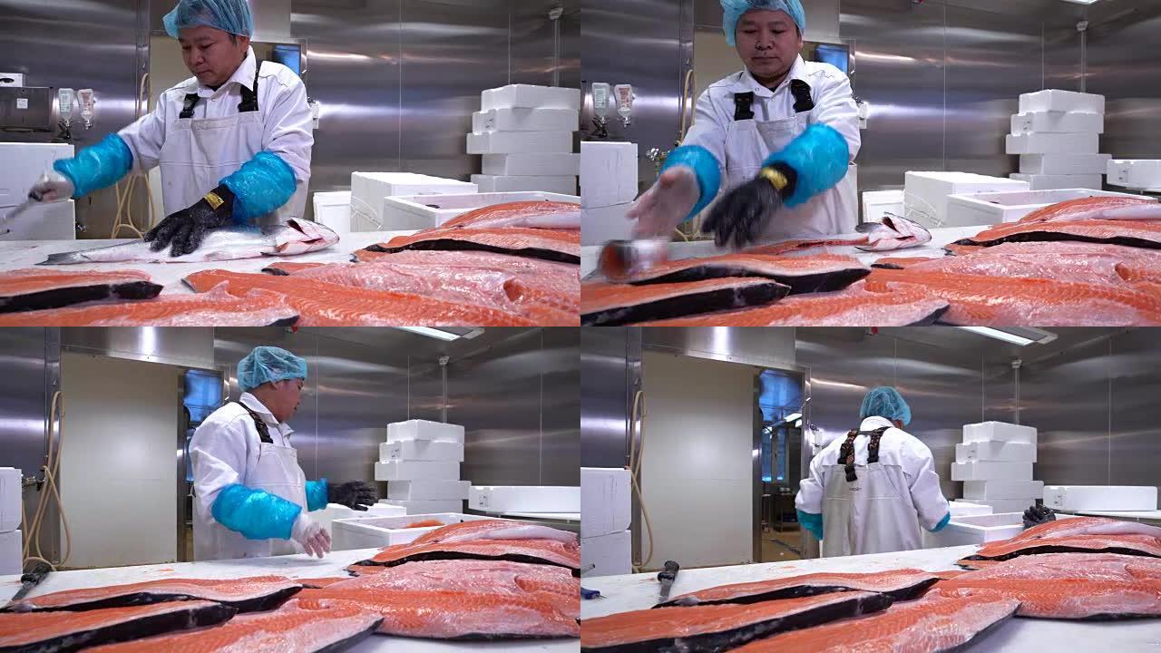 亚洲男子在鱼厂的餐桌上切鲑鱼片。多莉开枪