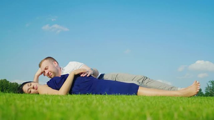 年轻的丈夫和怀孕的妻子在公园里放松，一起躺在绿色的草地上