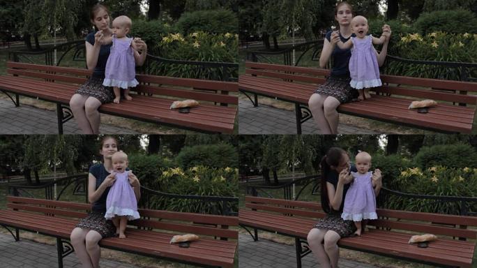 一个女孩用双手抱着一个女婴，女婴蹲下，好像在跳舞。旁边放着一条法国面包和智能手机