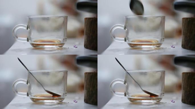 在肮脏的透明玻璃咖啡杯上放下茶勺的特写镜头浅景深