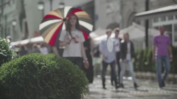 城市街道雨天的背景。实时。拿着五颜六色雨伞的年轻女孩。雨中带伞的人上下班。模糊的波克。自然背景