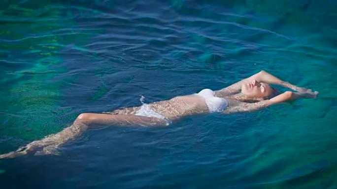 身穿白色比基尼的年轻幸福女人在蔚蓝的大海中游泳