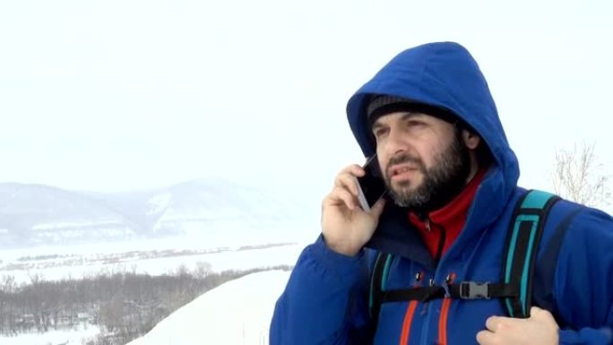 山上有胡子会说话的智能手机的旅行者。穿着夹克的白人男子在寻找全球定位系统信号。登山者冬季移动通信。冒