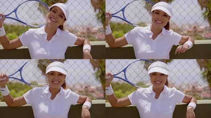 微笑的女人用网球拍靠在栅栏上