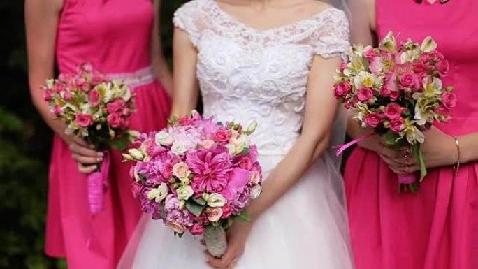 美丽的新娘站在粉红色礼服的伴娘之间，手里拿着玫瑰花束