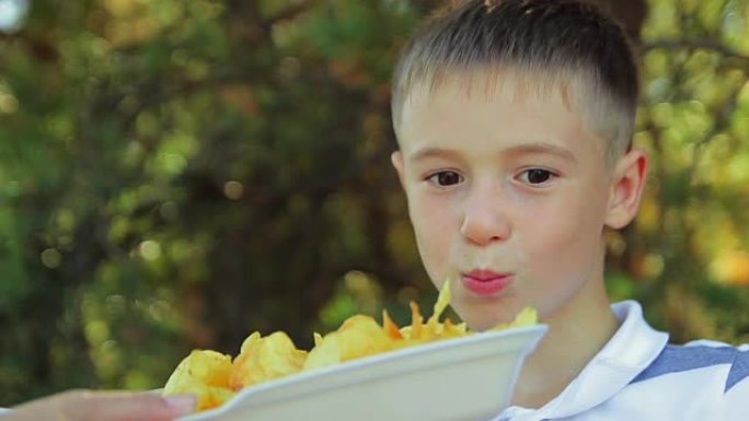 小男孩特写吃大自然公园里的金片，快餐不健康食品，儿童最好的食物，视频1080p