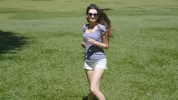 快乐的女孩在农村的绿草丛中奔跑，举手。年轻漂亮的女人在大自然的草坪上慢跑和旋转。自由概念慢动作后视图