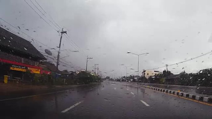 通过带有雨滴的汽车挡风玻璃的道路视图，在雨中行驶。