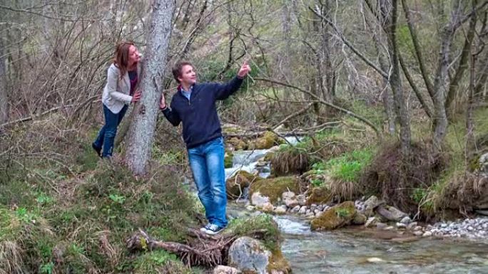 一对夫妇看着小溪边岩石附近的树，谁在美丽的风景中流动。