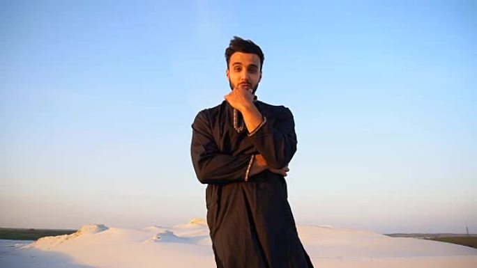 快乐的阿拉伯人肖像谁摆姿势和微笑看着相机，站在沙漠中间的露天晚上
