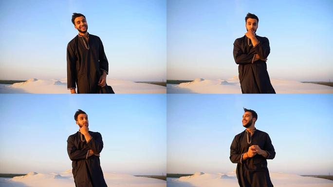 快乐的阿拉伯人肖像谁摆姿势和微笑看着相机，站在沙漠中间的露天晚上