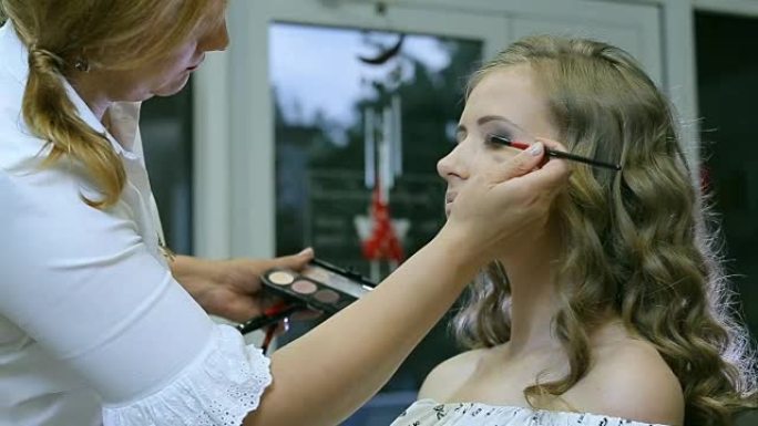 专业化妆师在金发模特眼睑上涂色调粉做眼影。