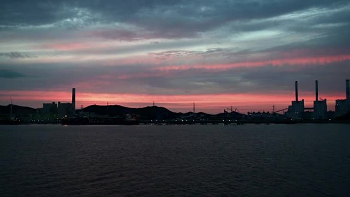 在暴风雨的海洋海岸线上，发电站和风力发电机的轮廓在日出或日落时带有辐射的火焰云。