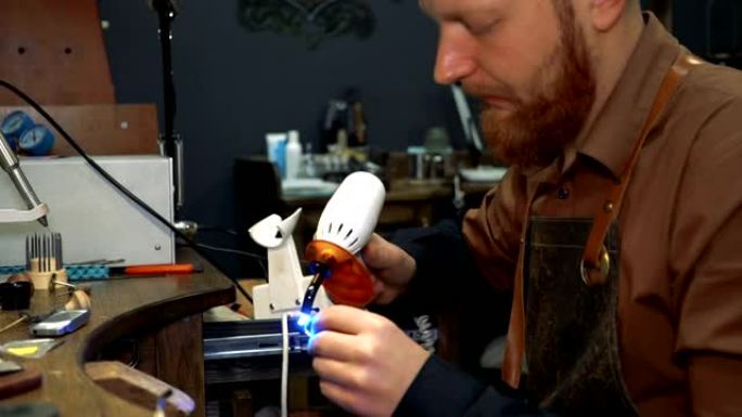 留着胡须的人拿着一个带有紫外线的装置，用于在银环上干燥搪瓷