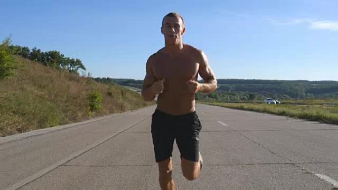 短跑运动员在高速公路上慢跑。男性运动运动员在夏季进行户外训练。年轻强壮的肌肉发达的家伙在锻炼期间在乡