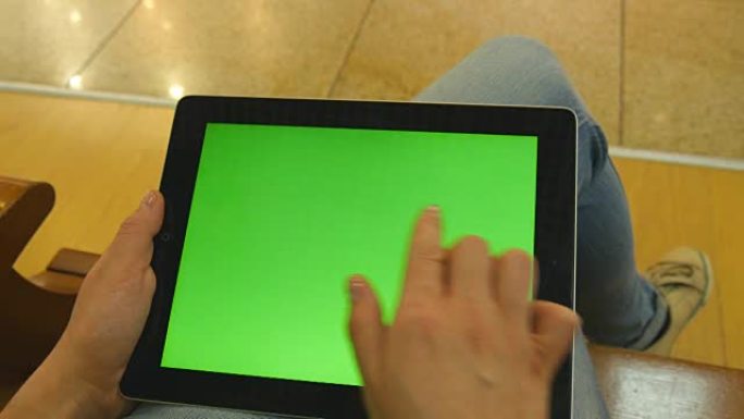年轻女孩坐在购物中心的长凳上，用平板电脑工作。女性双手使用绿屏平板电脑。色度键
