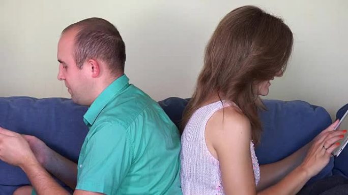 夫妻使用自己的平板电脑背靠背坐在沙发上