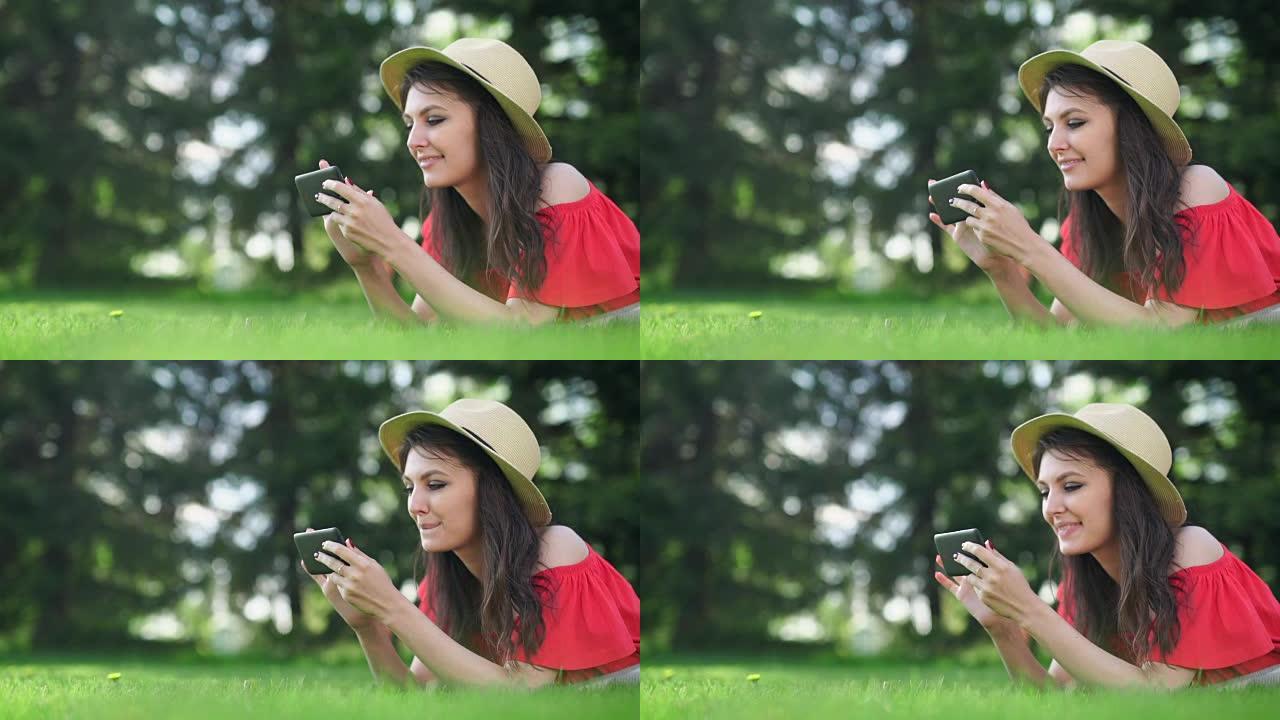 年轻女子用手机空红屏躺在绿草地上。