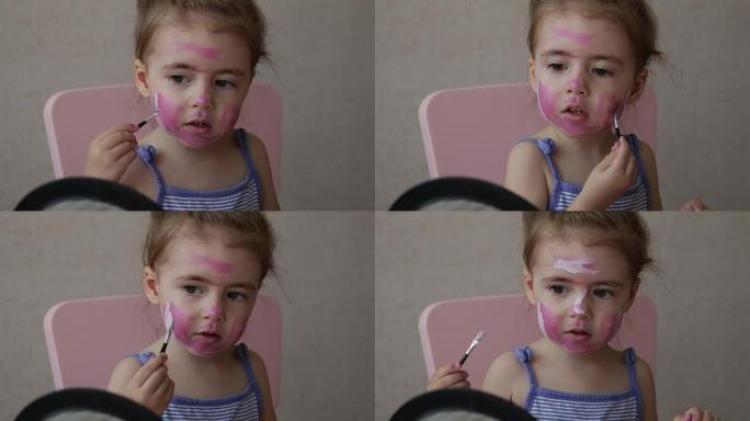 金发三岁的婴儿看着镜子在脸上画彩色条纹