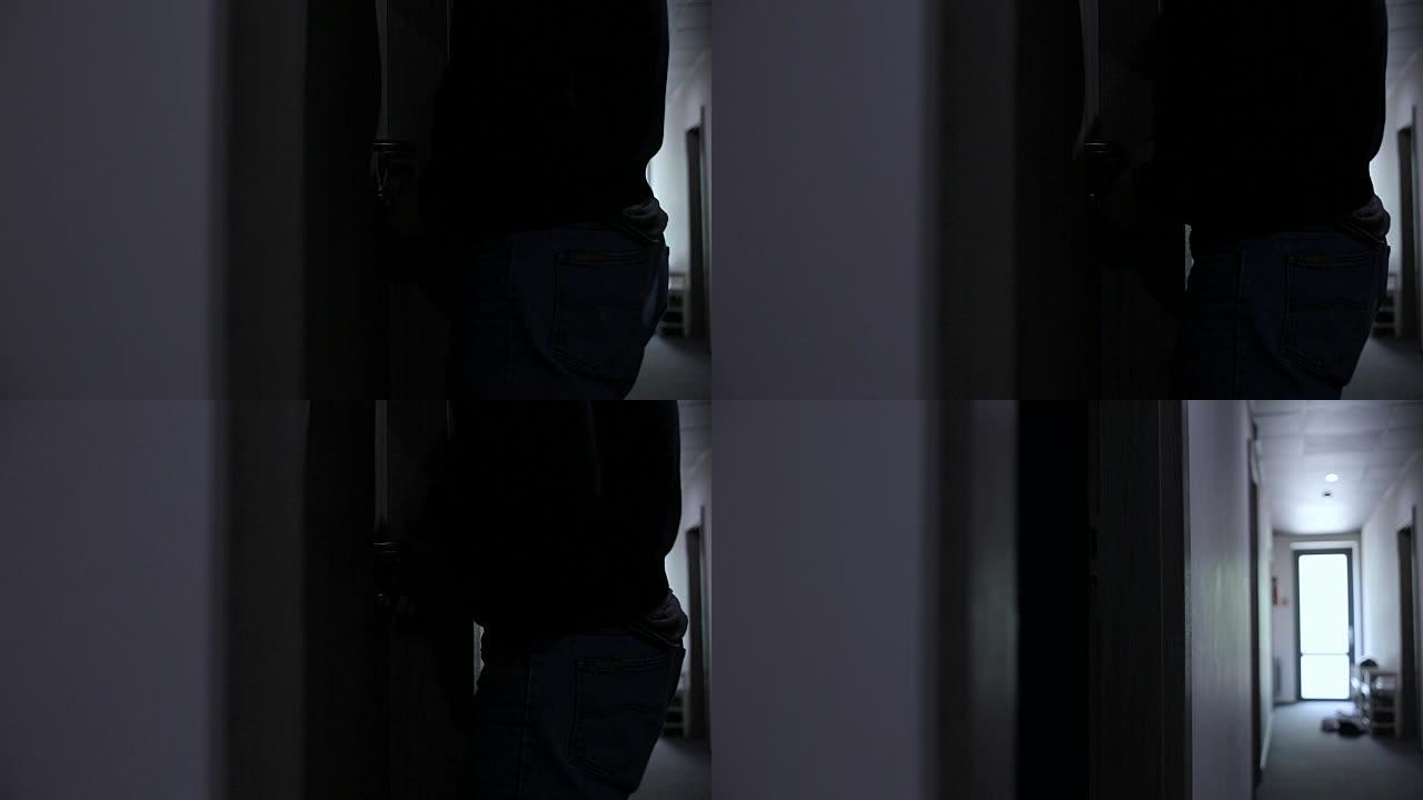 男子小偷在黑暗的走廊上打破了公寓的门