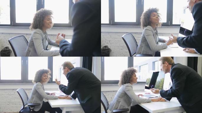 女商人在现代开放式办公室与在计算机上工作的老板交谈，两个商人讨论想法快乐的微笑