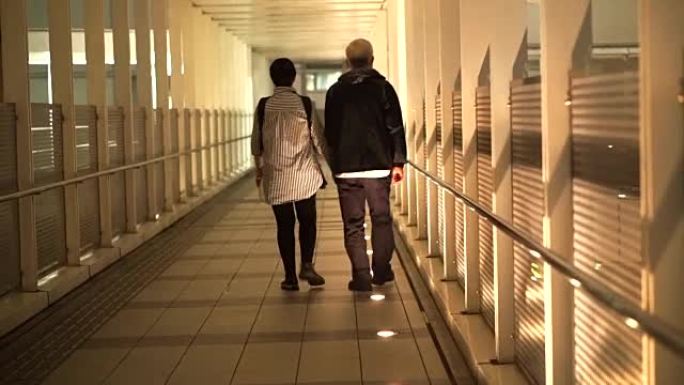 亚洲老年退休夫妇手牵着手沿着从火车站到公寓的掩护走道行走
