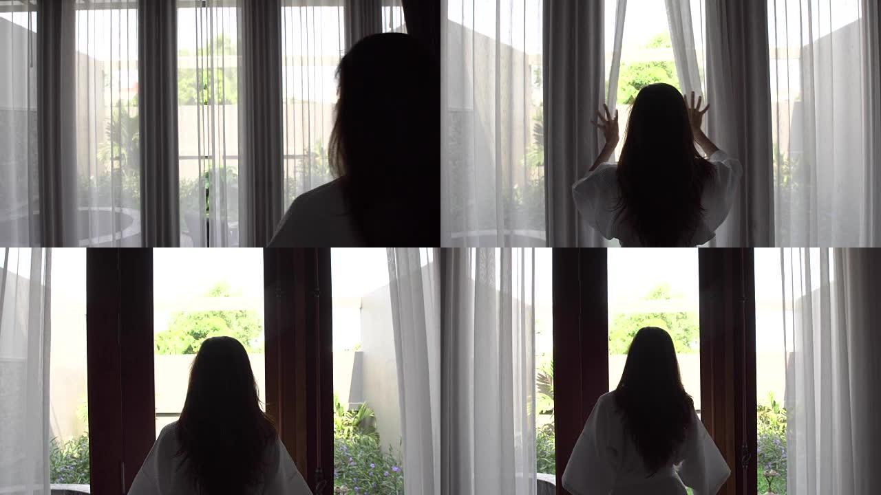 穿着浴袍的年轻女子打开窗帘，看着站在她家窗户附近的花园，看着镜头。