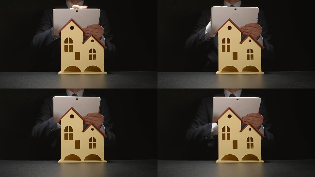 商人拿着平板电脑放在桌子上的房屋模型后面