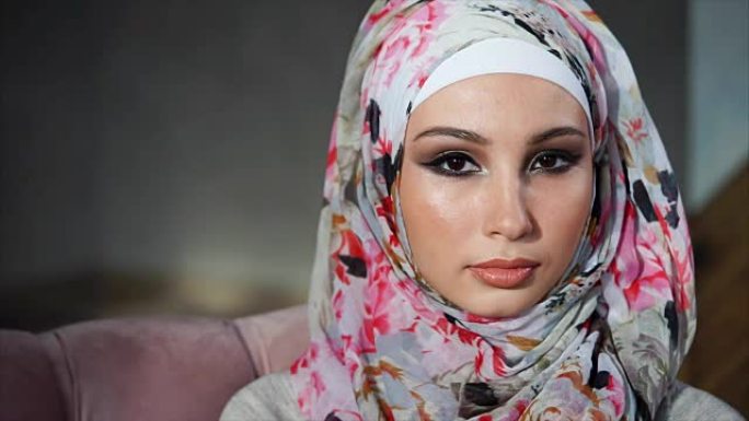 年轻的穆斯林妇女，戴着头巾的眼睛，看着相机，慢慢地眨眼